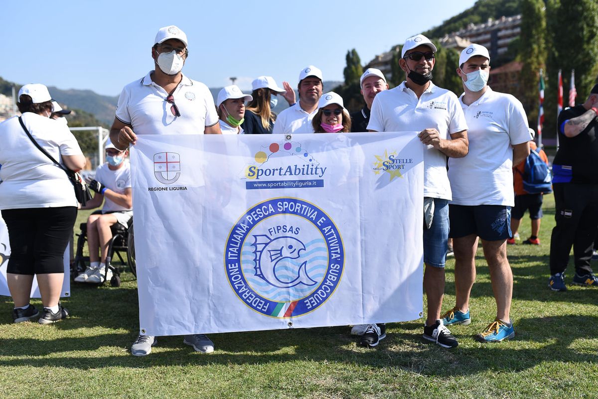 a figura intera persone del Centro che reggono la bandiera FIPSAS dello SportAbility in maglia e cappellino bianchi