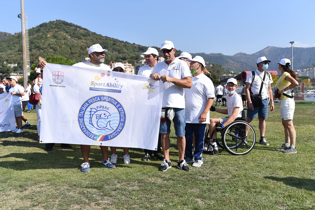 persone del Centro che reggono lo striscione FIPSAS dello SportAbility in maglia e cappellino bianchi sul prato